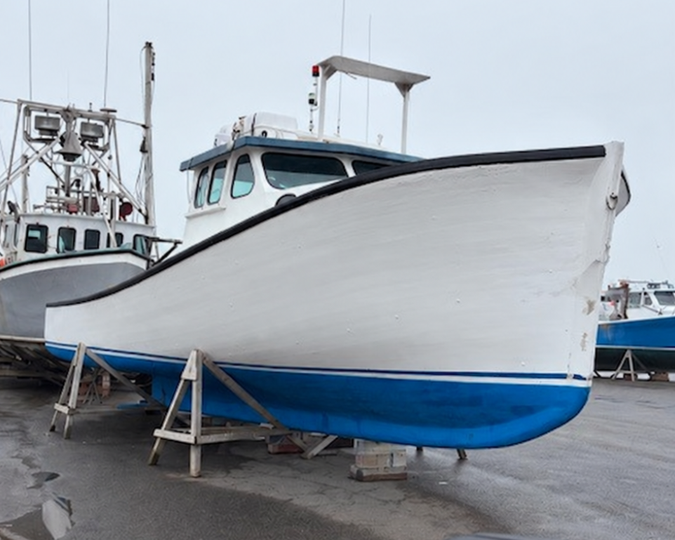 A white and blue fishing boat on a boat lift in a wet boatyard, with another boat and a vehicle mirror visible in the background and foreground.