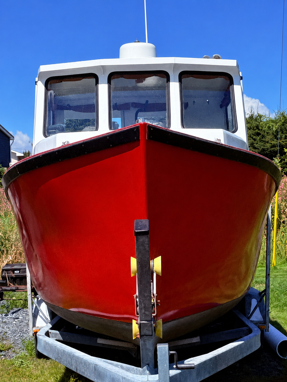A red and white boat on a metal trailer, photographed outdoors against a blue sky with grass and trees visible in the background.