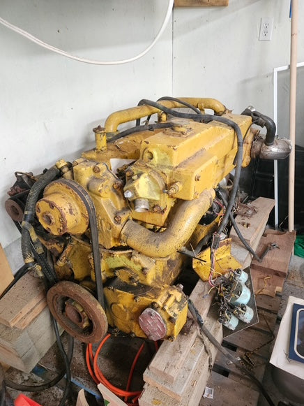 A large used yellow industrial engine mounted on a wooden pallet in a cluttered workshop or garage setting.