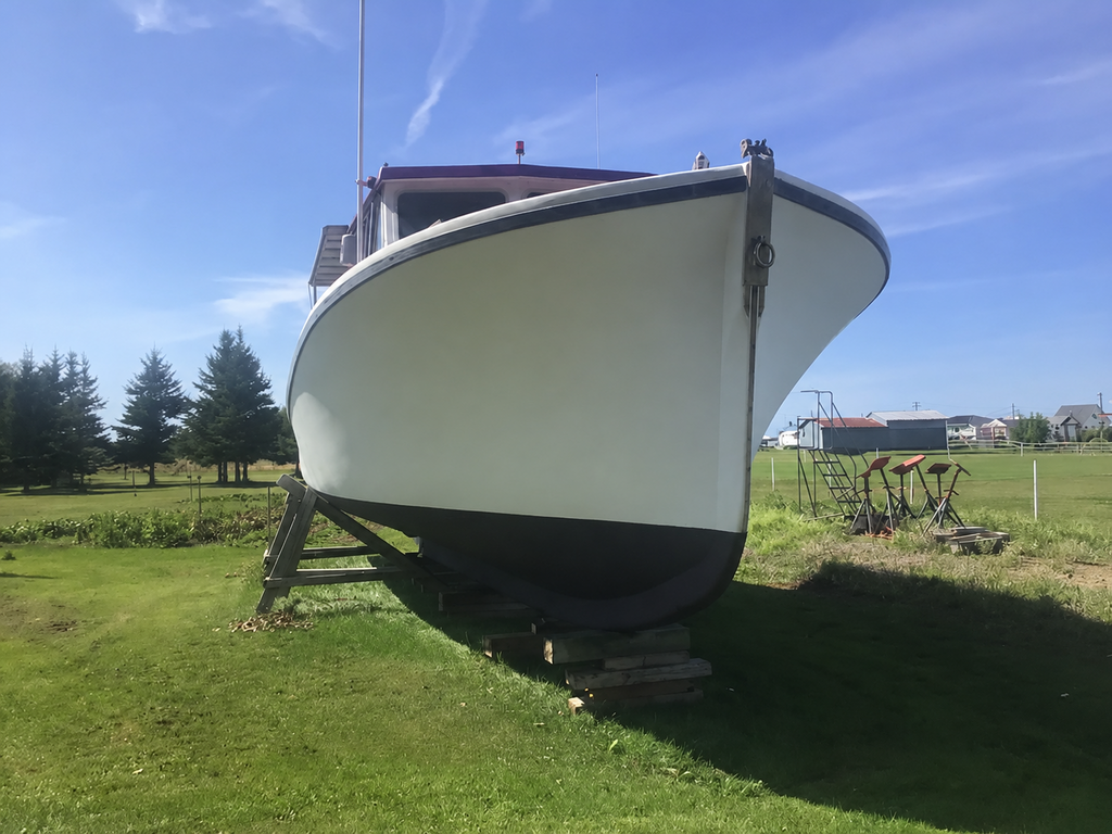 A white boat hull on a wooden lift in an outdoor grassy field under a blue sky with trees in the background.