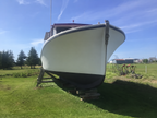 A white boat hull on a wooden lift in an outdoor grassy field under a blue sky with trees in the background.