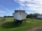 A white boat photographed from the front in an outdoor grassy area under a blue sky, supported by wooden boat stands.