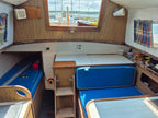 Interior of a small boat cabin with wooden walls, blue cushions, and a window view.