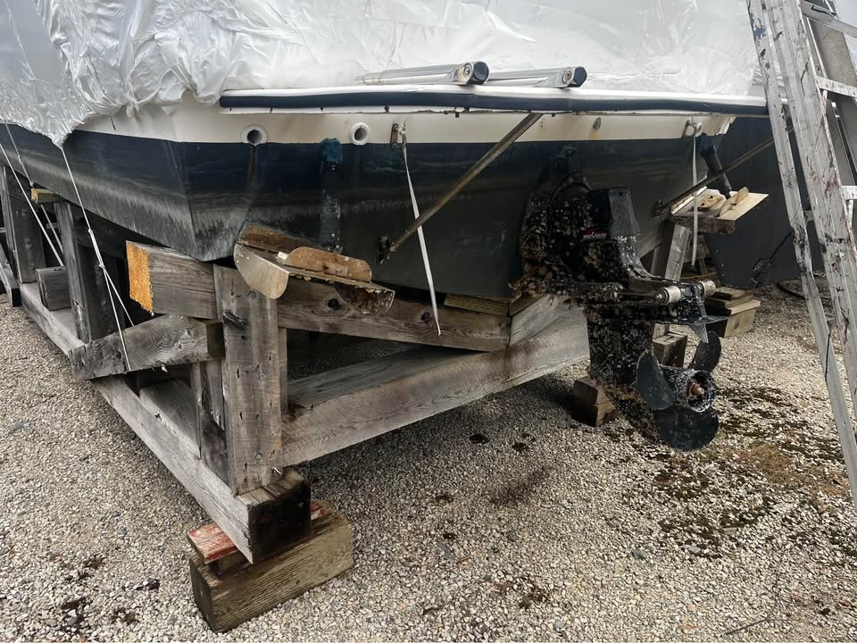 Boat on a wooden pallet with a tarp covering it, on a concrete surface.
