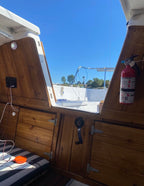 Interior of a boat cabin with wooden paneling, a fire extinguisher, and a view of water and sky.