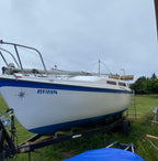 White sailboat with blue stripe on a trailer in a grassy area