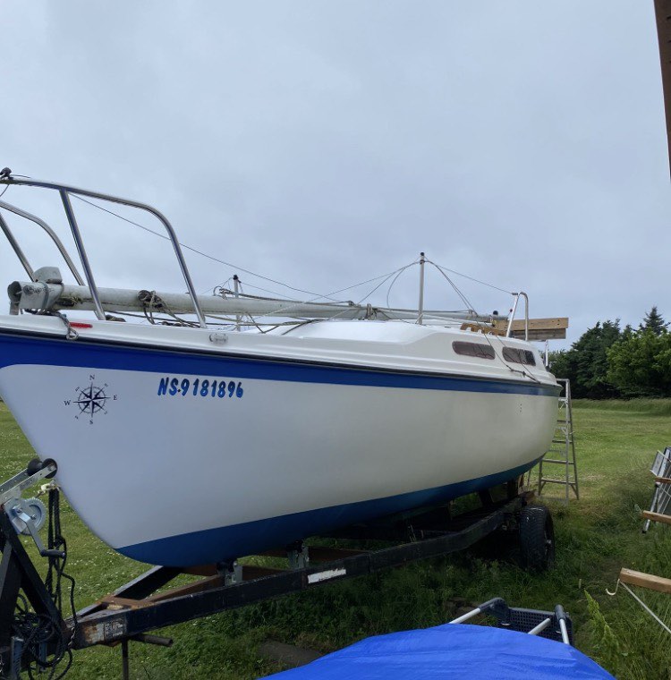 White sailboat with blue stripe on a trailer in a grassy area
