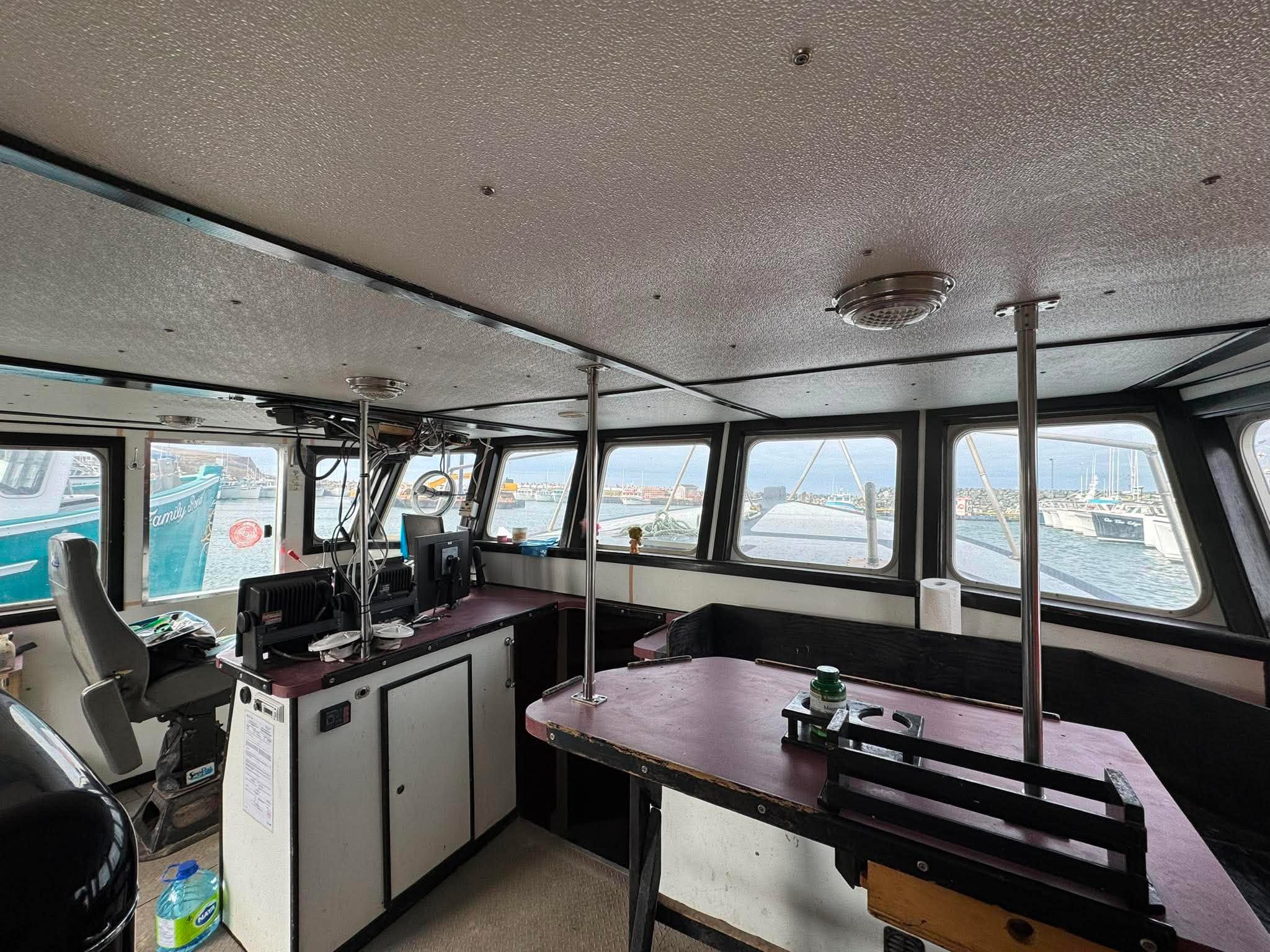 Interior of a boat with steering wheel, dashboard, and large windows showing water outside.