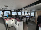 Interior of a boat with control panels and seating area, windows showing water view.