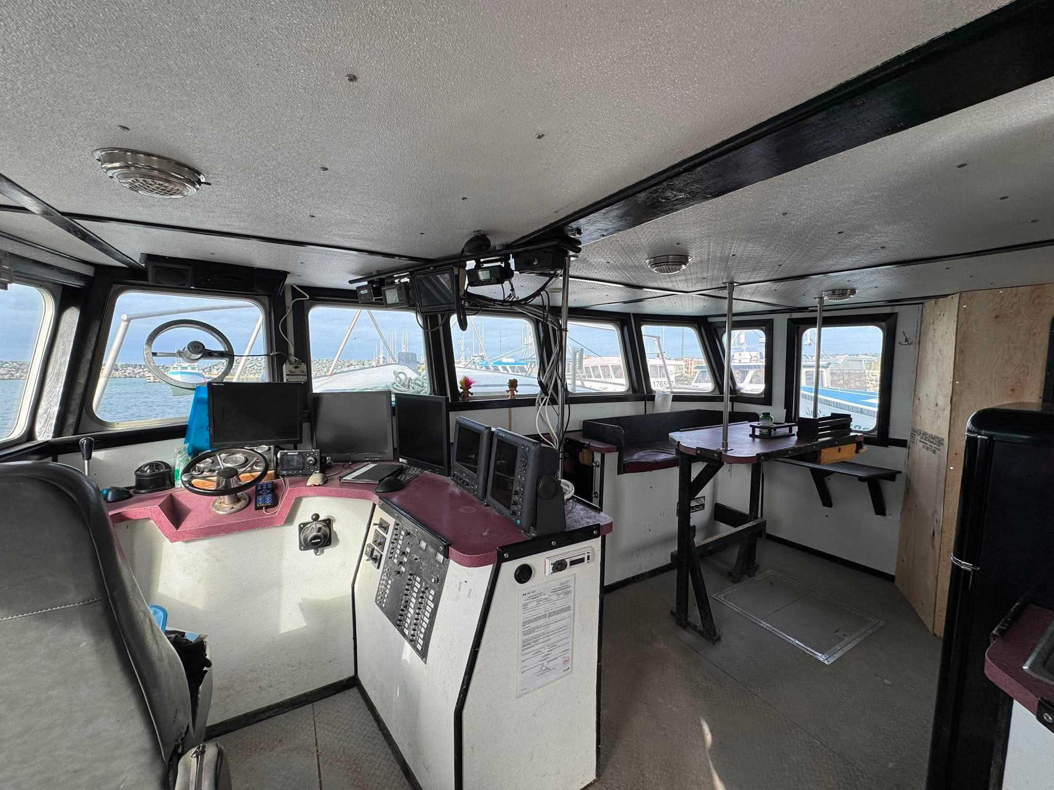 Interior of a boat with control panels and seating area, windows showing water view.