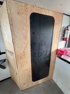 Wooden panel with a black mat attached, likely in a workshop or storage area.