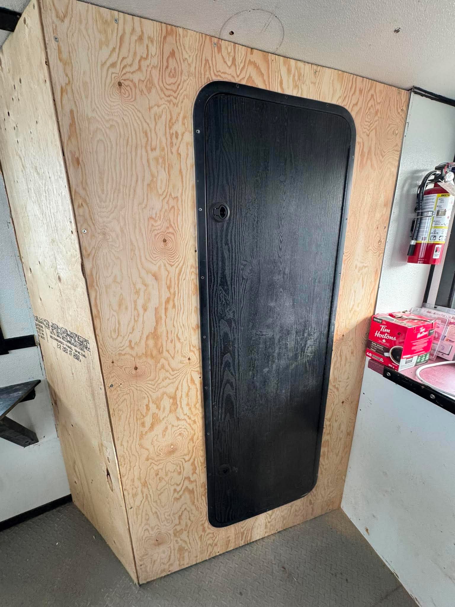 Wooden panel with a black mat attached, likely in a workshop or storage area.