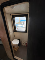 Small bathroom with a toilet and window, viewed from outside through a door.