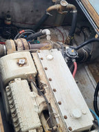 A close-up view of a used marine diesel engine, likely a Mercury outboard, showing the silver and off-white metal engine block, hoses, and mechanical components inside a boat engine bay.