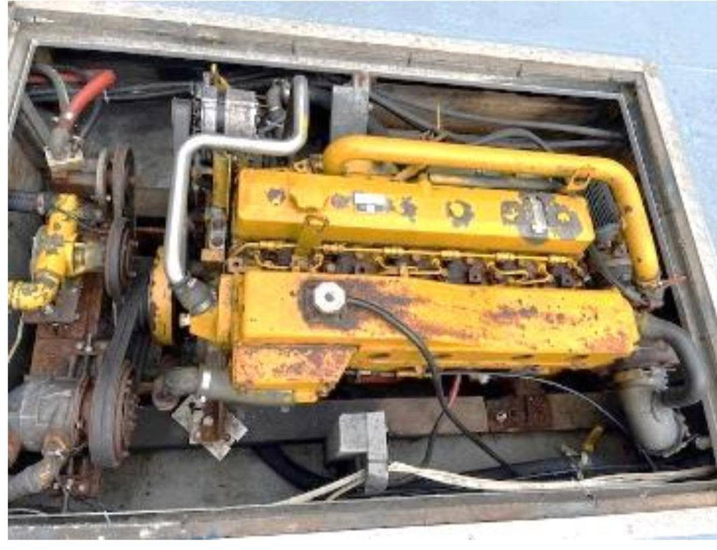 A large yellow industrial engine mounted inside a metal enclosure, with visible hoses, pipes, belts, and rusted wear on the painted surface.