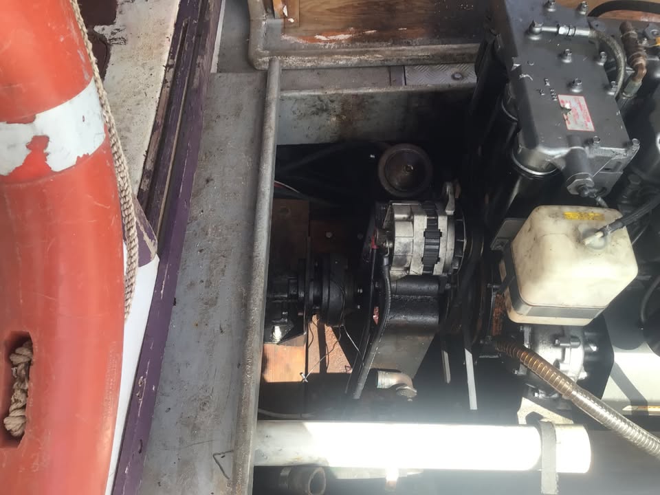Close-up of a boat engine compartment showing the alternator, battery, and various mechanical components inside a metal engine bay.