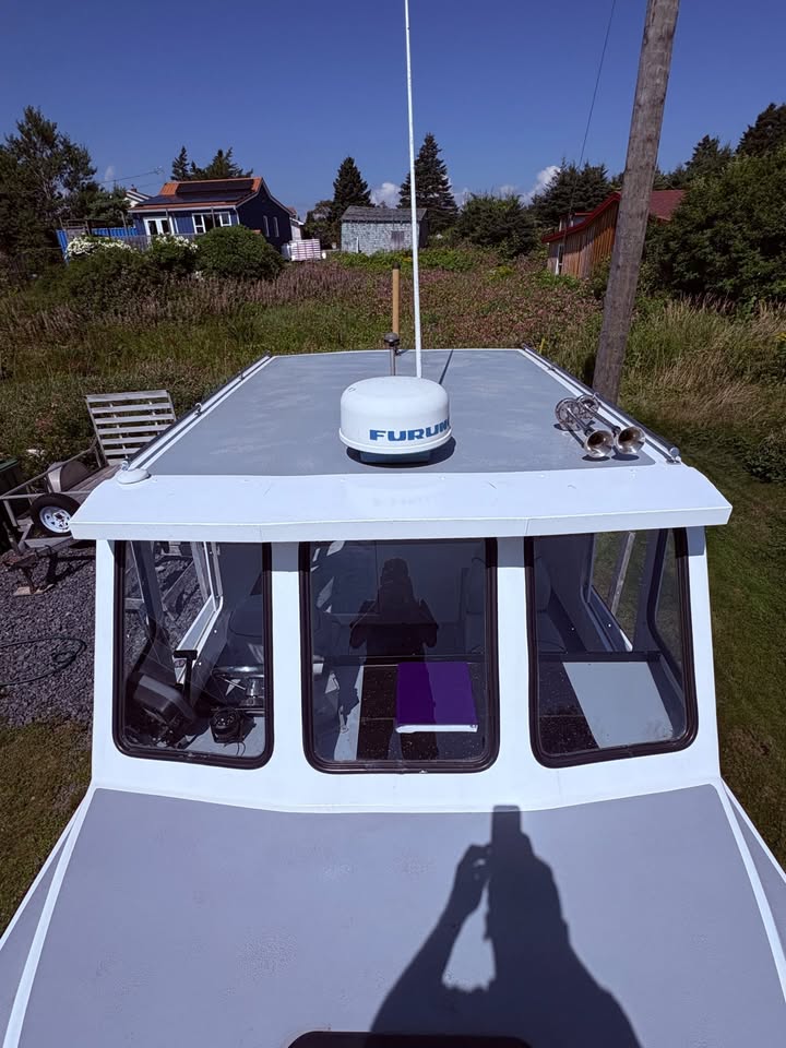 A white boat cabin top with a gray roof section, featuring a white and blue Fuzoom radar antenna on top, photographed outdoors on a grassy lawn with houses and trees in the background.