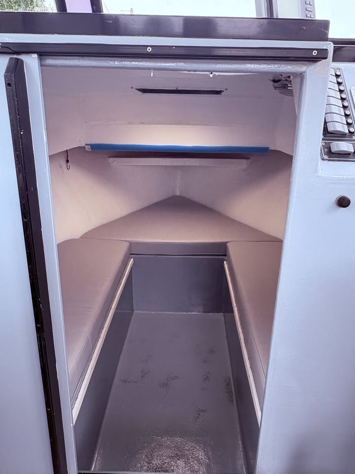 The open front door of a boat cabin or storage compartment, showing a gray floor and light gray walls with a blue strip near the ceiling.