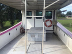 The back deck of a white boat or vessel with a gray metal storage box in the center, an orange life preserver, and a purple stripe along the side, photographed outdoors.