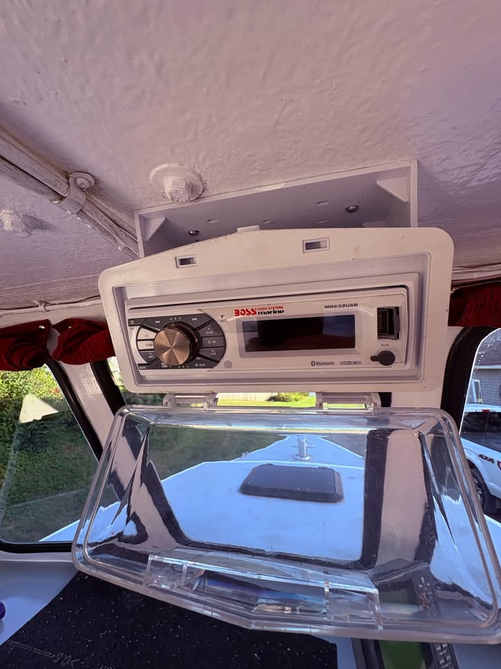 A white Bose wireless stereo system mounted on a wall inside a vehicle, with a clear plastic storage tray hanging below it.