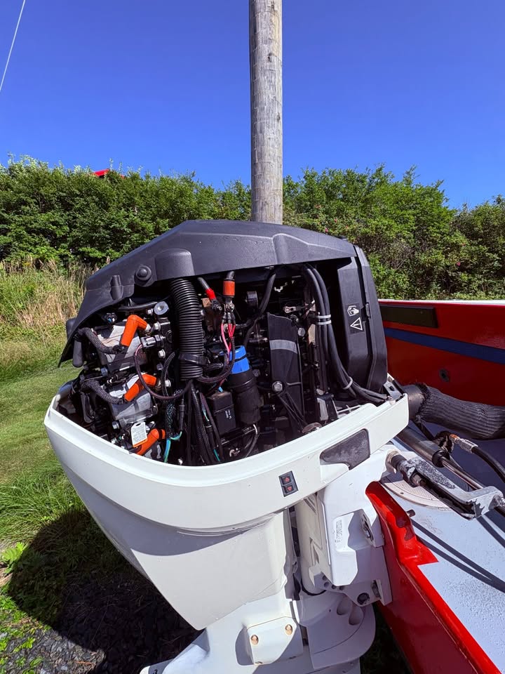 A white and black outboard motor boat engine shown open, revealing internal components, mounted on the side of a red and gray boat outdoors under a blue sky.