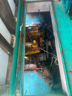 A close-up view of a used yellow and black marine engine or generator engine compartment, showing the engine block, belts, hoses, and wiring inside a teal painted metal housing.