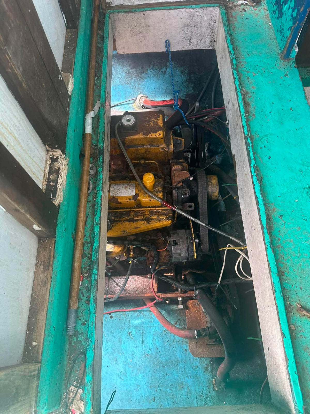 A close-up view of a used yellow and black marine engine or generator engine compartment, showing the engine block, belts, hoses, and wiring inside a teal painted metal housing.