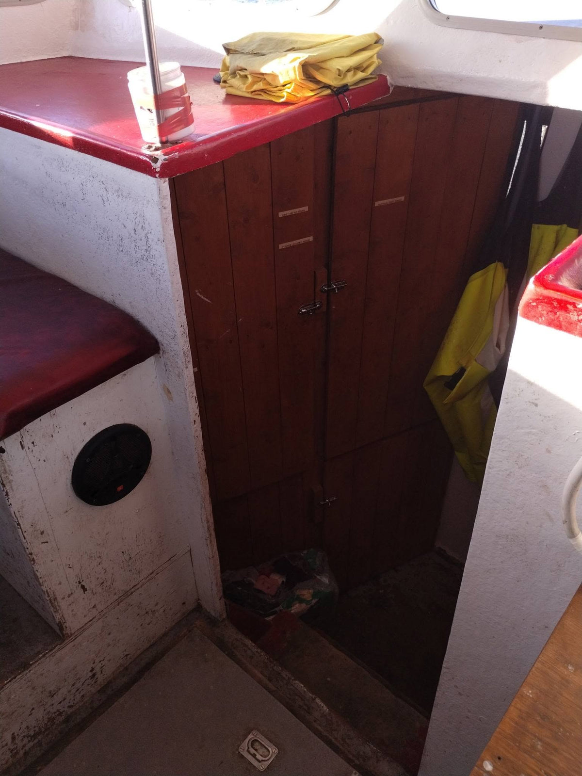 A narrow interior space with dark reddish-brown wooden cabinets or drawers, a red top surface, white worn metal or painted sides, and a yellow fabric item hanging on the right. The photo appears to show the product in a real environment rather than as a clean studio shot.