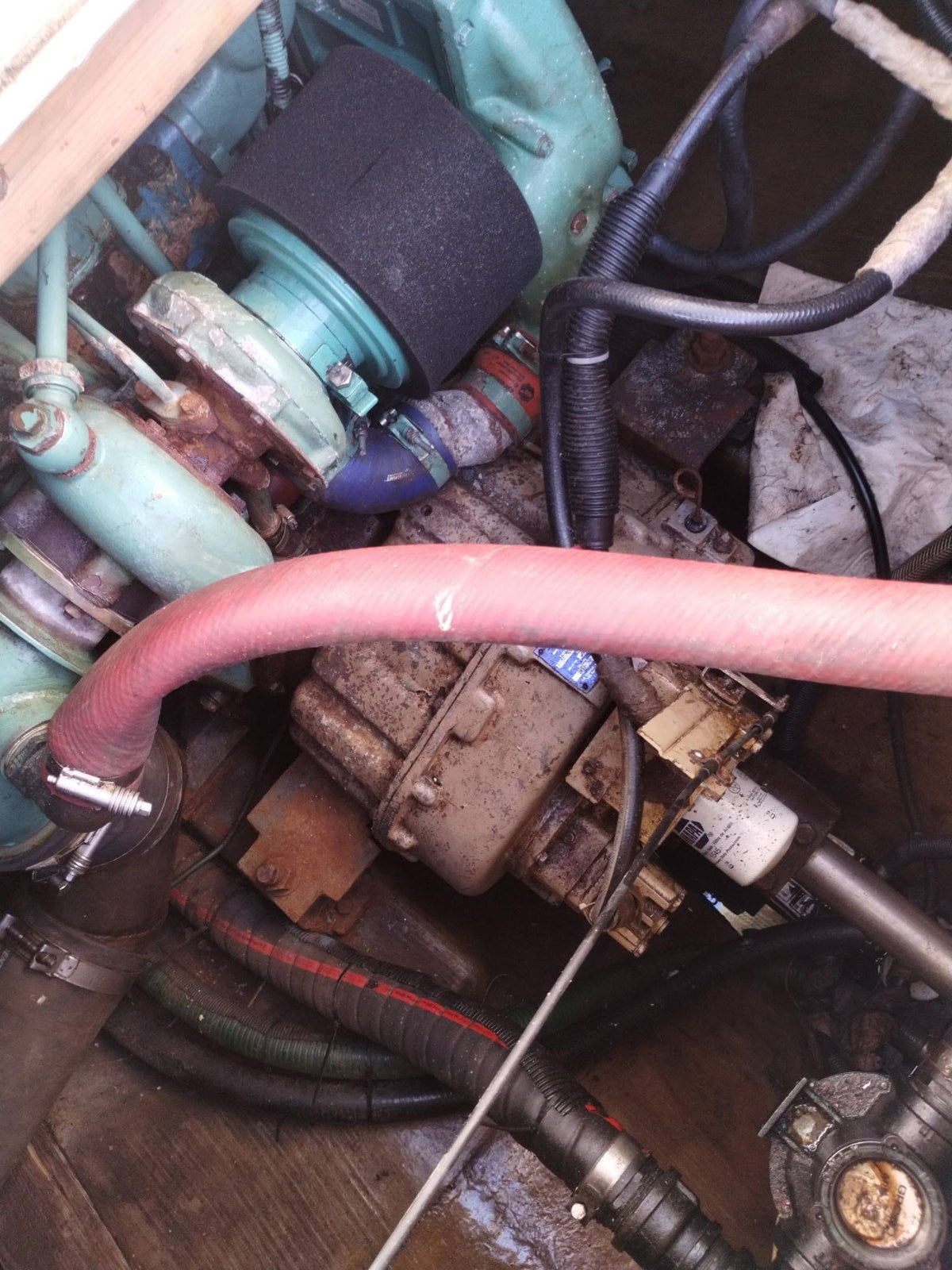 Close-up of a used marine engine component, showing a turquoise painted engine block, a black foam air filter, a dusty metal manifold, and a prominent pink/red rubber intake hose.