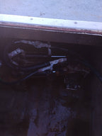 A close-up view of mechanical hydraulic hoses and metal components inside a dark compartment, likely a boat or machinery housing.
