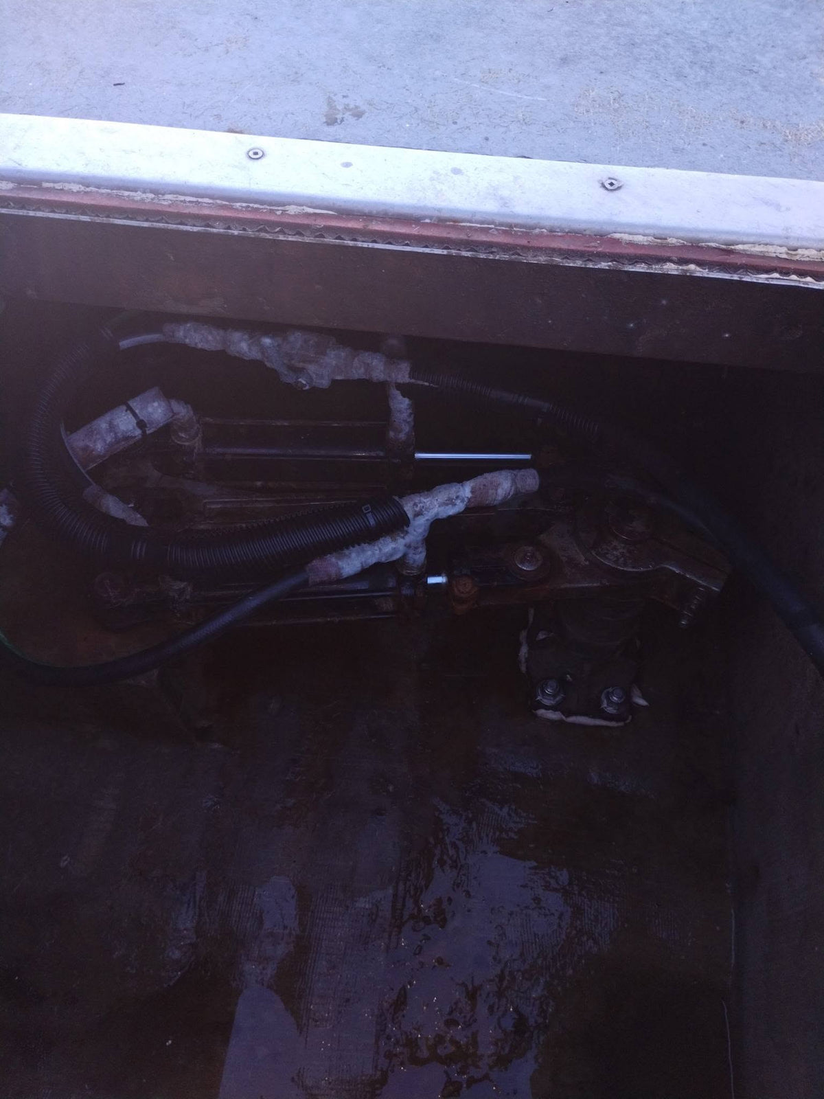A close-up view of mechanical hydraulic hoses and metal components inside a dark compartment, likely a boat or machinery housing.