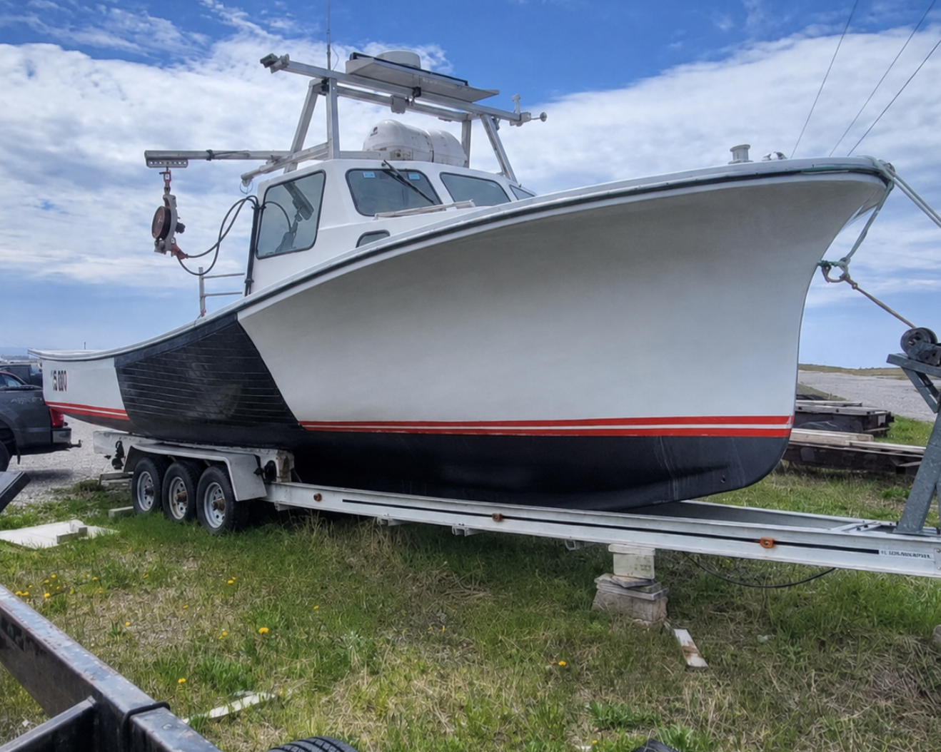 A white and black fishing boat on a trailer outdoors on grass under a blue sky with clouds.