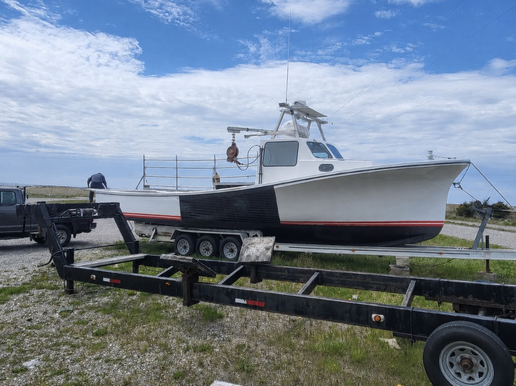 A white fishing boat with a black hull and red stripe, shown on a black trailer outdoors under a blue sky with clouds.