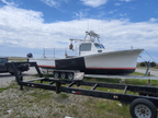 A white fishing boat with a black hull and red stripe, shown on a black trailer outdoors under a blue sky with clouds.
