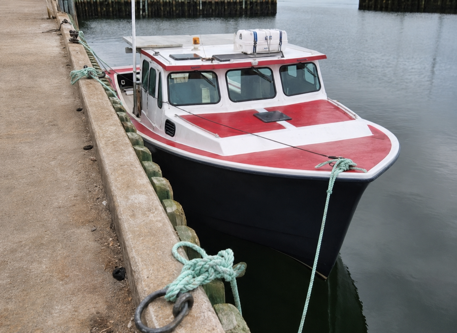 Red and white boat tied to a dock with a calm water background