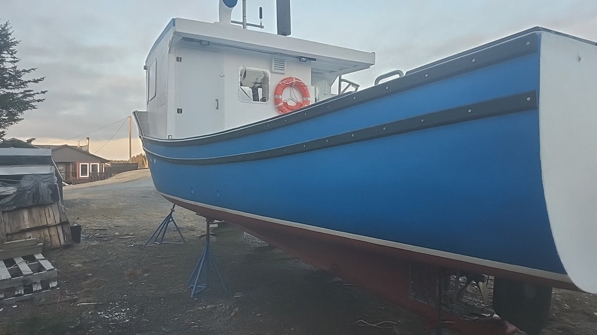 A blue and white fishing boat on a trailer outdoors, photographed in a workshop or yard setting with a cloudy sky.