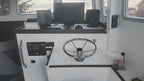 The helm station of a boat featuring a chrome steering wheel, white control panels, navigation screens, and instruments.