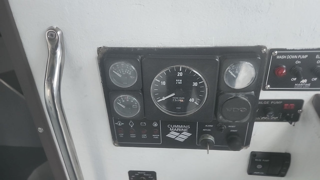 A Cummins Marine instrument panel with multiple gauges and controls mounted on a white surface, next to a chrome handle.