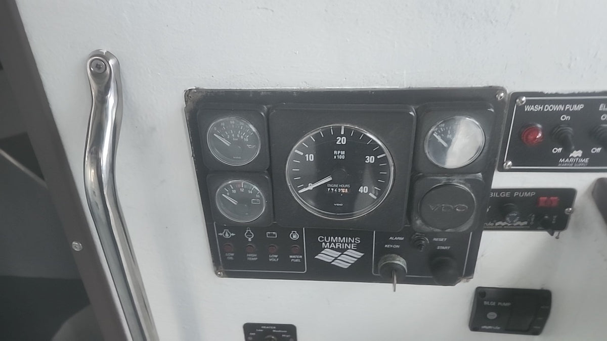 A Cummins Marine instrument panel with multiple gauges and controls mounted on a white surface, next to a chrome handle.