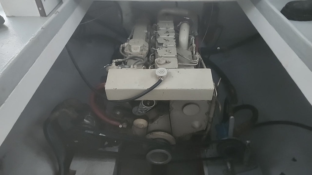 A close-up view of a boat's engine housed within a gray fiberglass compartment, showing the engine block, belts, and wiring.