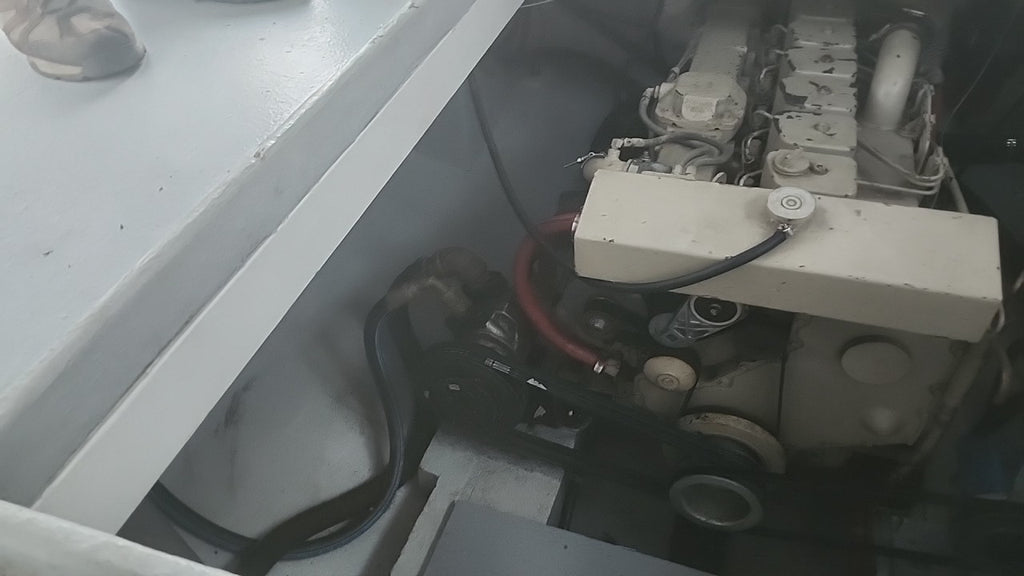 Close-up of a boat engine compartment showing the engine block, hoses, and mechanical components inside a white boat cabin.
