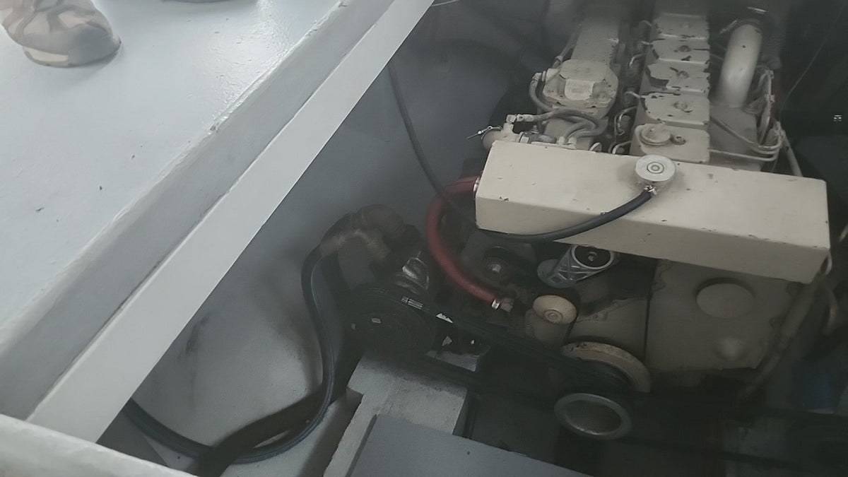 Close-up of a boat engine compartment showing the engine block, hoses, and mechanical components inside a white boat cabin.