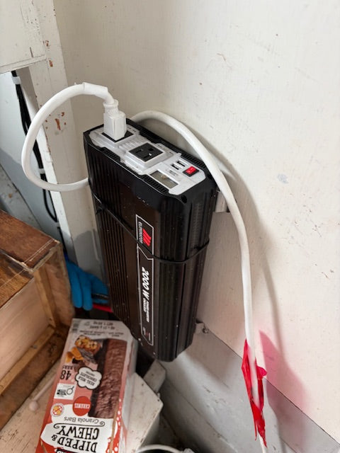 A black and white electric trolling motor mounted on a white wall, with a white power cord plugged in. A box of Dipped Chewy Dipped Cheeks gummy candies is visible on the floor below.
