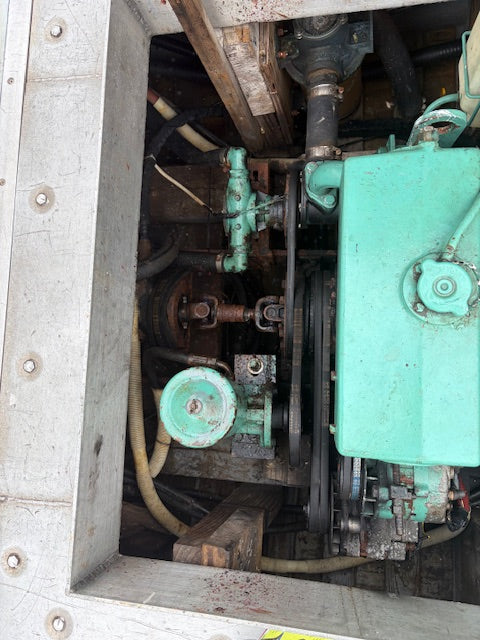 A close-up view of an industrial engine or machinery component with a large mint green metal housing, belts, hoses, and surrounding mechanical parts inside a metal enclosure.