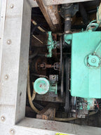 A close-up view of an industrial engine or machinery component with a large mint green metal housing, belts, hoses, and surrounding mechanical parts inside a metal enclosure.