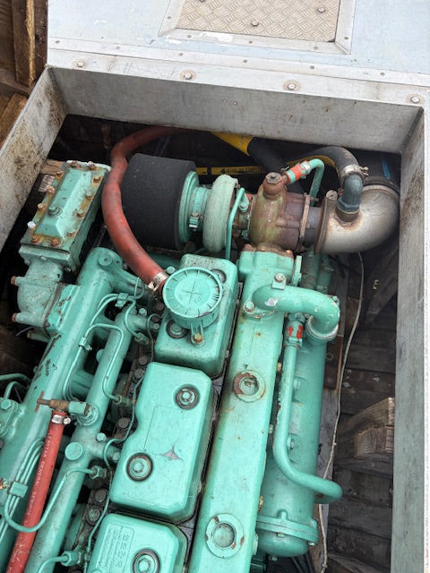 A close-up view of a large industrial engine housed inside a metal casing, featuring a prominent mint green painted engine block with various pipes, hoses, and mechanical components visible.