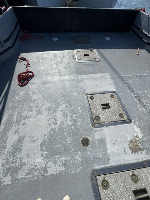 Close-up of a weathered gray metal deck with diamond-plate hatch covers, a red rope, and a dark vertical panel on the left.
