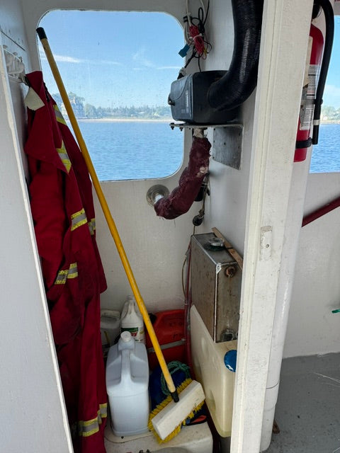 A red life jacket with yellow reflective stripes hanging in the cockpit of a boat, alongside a yellow-handled brush and other nautical equipment.