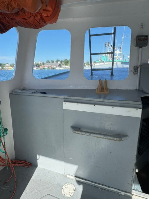 An interior view of a boat cabin showing a gray door with a metal handle, three arched windows looking out onto blue water and boats, and some ropes on the deck.