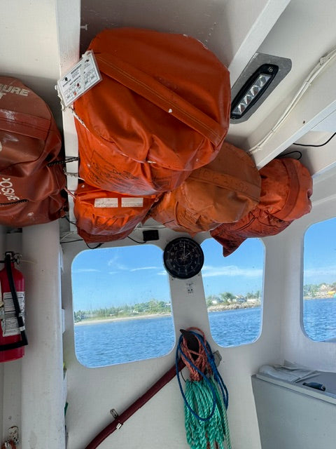 Several orange and brown waterproof gear bags packed with documents, secured inside a white boat cabin with windows showing blue water and shoreline outside.